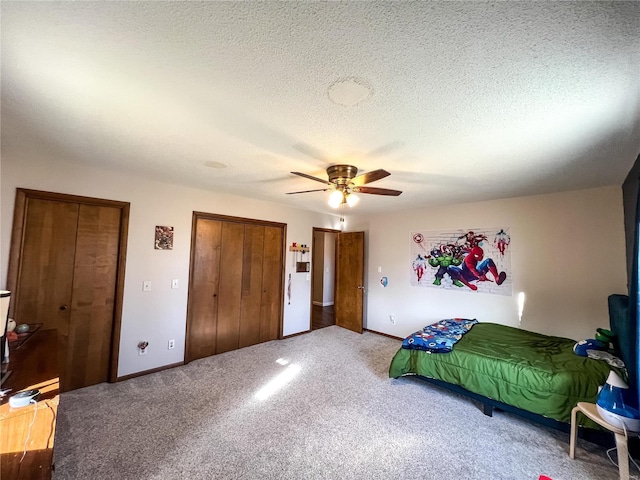 bedroom with carpet flooring, multiple closets, baseboards, a ceiling fan, and a textured ceiling