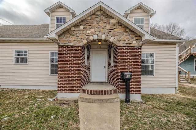 entrance to property with stone siding, roof with shingles, and a yard