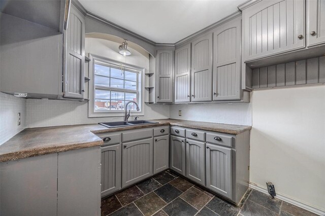 kitchen with gray cabinetry, a sink, stone tile flooring, tasteful backsplash, and arched walkways