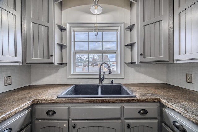 kitchen featuring a sink, gray cabinetry, open shelves, dark countertops, and tasteful backsplash