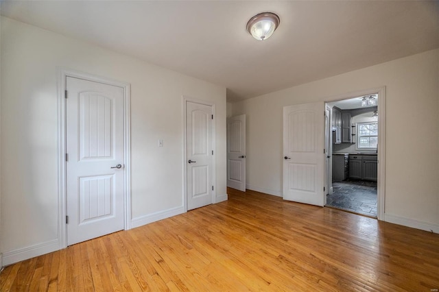 unfurnished bedroom featuring light wood-style flooring, baseboards, and connected bathroom