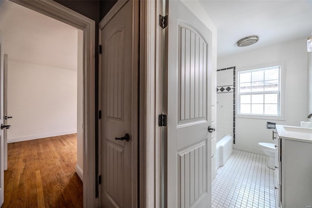 full bathroom with vanity, toilet, baseboards, washtub / shower combination, and wood finished floors