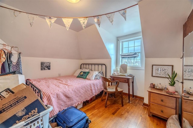 bedroom with light wood-type flooring, vaulted ceiling, and baseboards