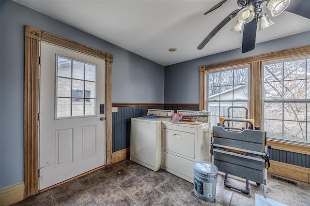 washroom featuring washing machine and dryer, baseboards, ceiling fan, wainscoting, and dark stone finish flooring