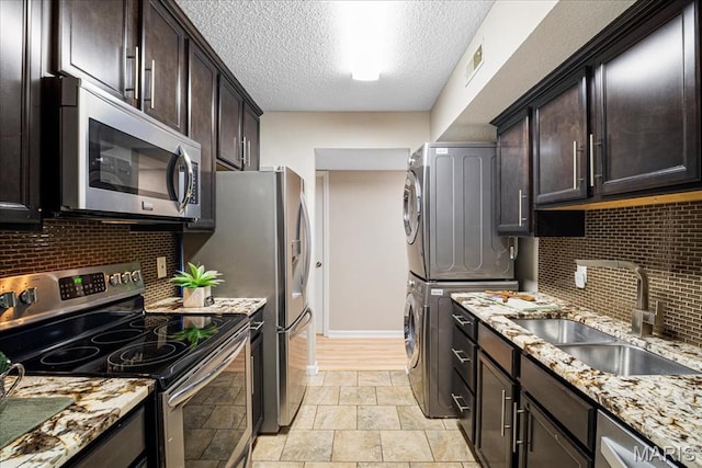 1528 Thrush Ter, Brentwood, MO 63144 - kitchen featuring appliances with stainless steel finishes, stacked washing machine and dryer, a sink, decorative backsplash, and light stone finish floors
