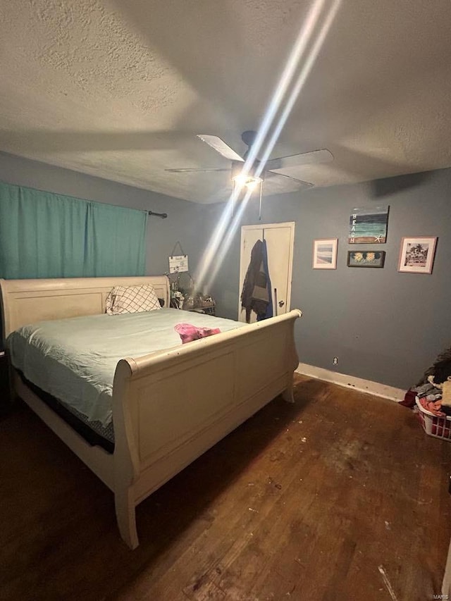 bedroom with dark wood-type flooring, a textured ceiling, ceiling fan, and baseboards