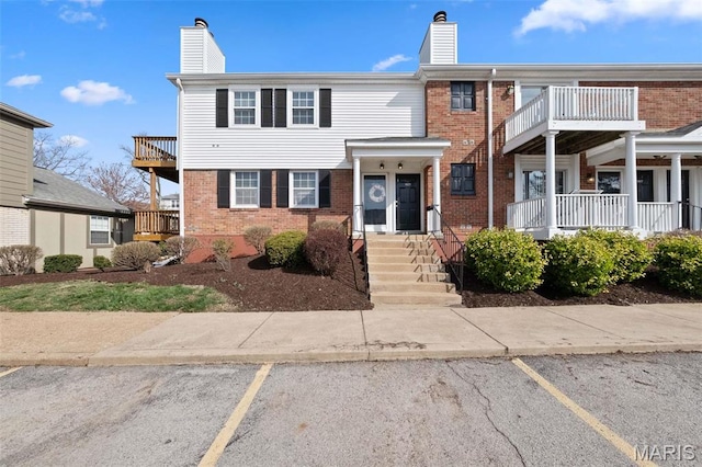 view of property with a chimney, uncovered parking, brick siding, and a balcony