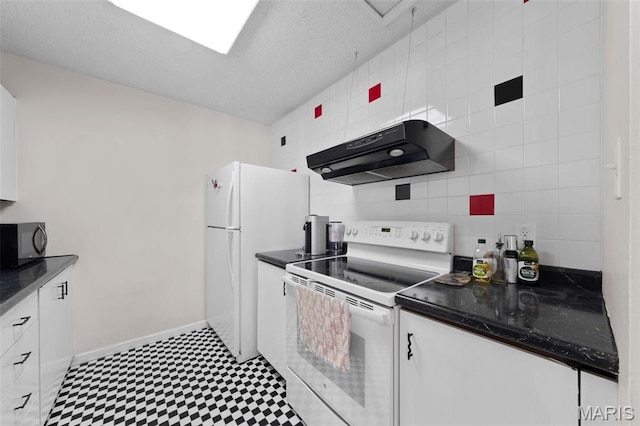 kitchen with white appliances, under cabinet range hood, tile patterned floors, dark countertops, and white cabinets