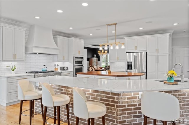 261 US Dr, Wentzville, MO 63385 - kitchen featuring appliances with stainless steel finishes, a large island, premium range hood, wooden counters, and a sink