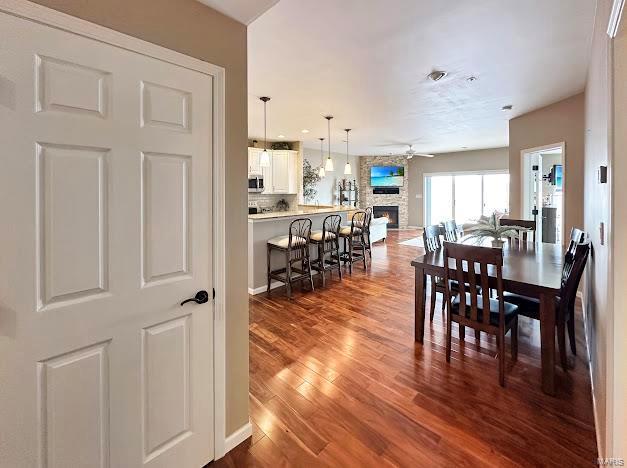 dining space featuring wood finished floors, a ceiling fan, and a stone fireplace