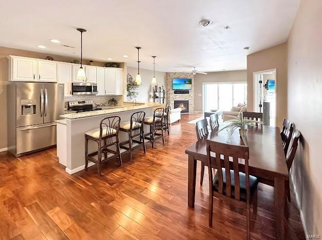 dining space with a ceiling fan, a stone fireplace, wood finished floors, and recessed lighting