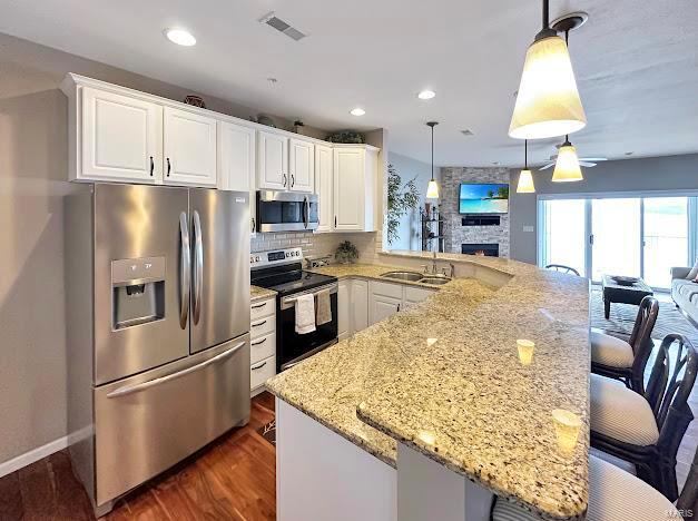 kitchen with stainless steel appliances, open floor plan, dark wood-style flooring, a stone fireplace, and a peninsula
