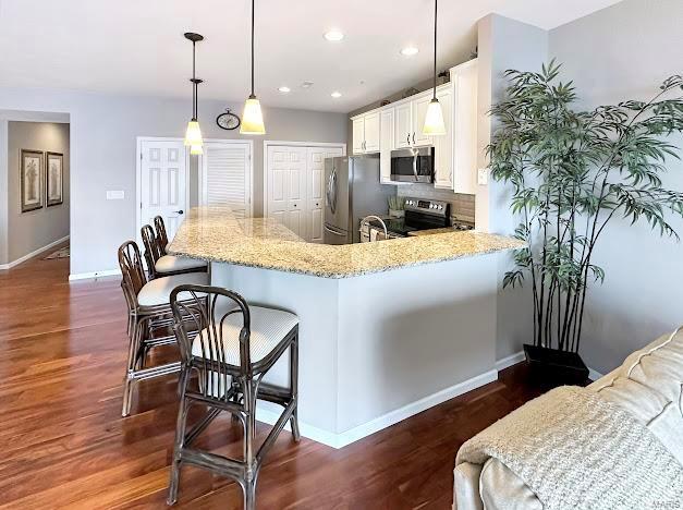 kitchen with stainless steel appliances, baseboards, dark wood finished floors, light stone counters, and a breakfast bar area