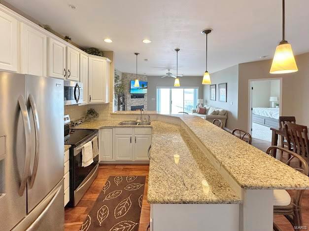 kitchen with appliances with stainless steel finishes, a sink, wood finished floors, a breakfast bar, and a ceiling fan