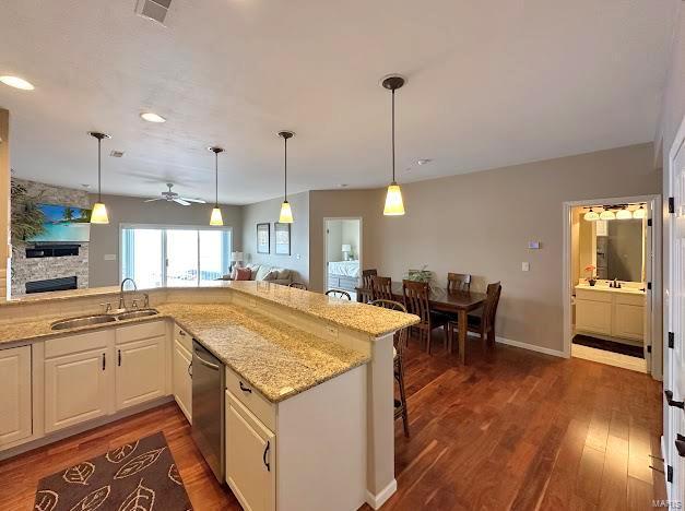 kitchen featuring a sink, dishwasher, a fireplace, dark wood finished floors, and light stone counters