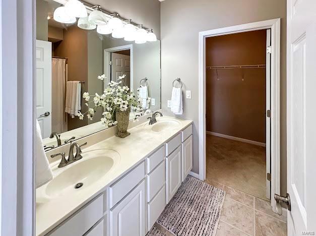full bathroom featuring tile patterned floors, a spacious closet, double vanity, and baseboards