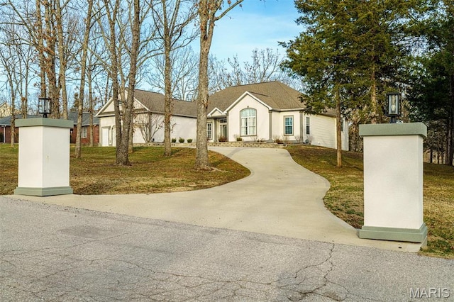 view of front of property with curved driveway, stucco siding, a front lawn, and roof with shingles