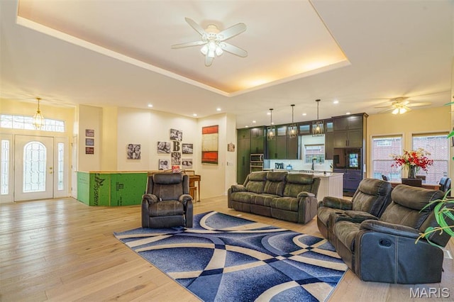 living area featuring a ceiling fan, a raised ceiling, light wood-style flooring, and recessed lighting