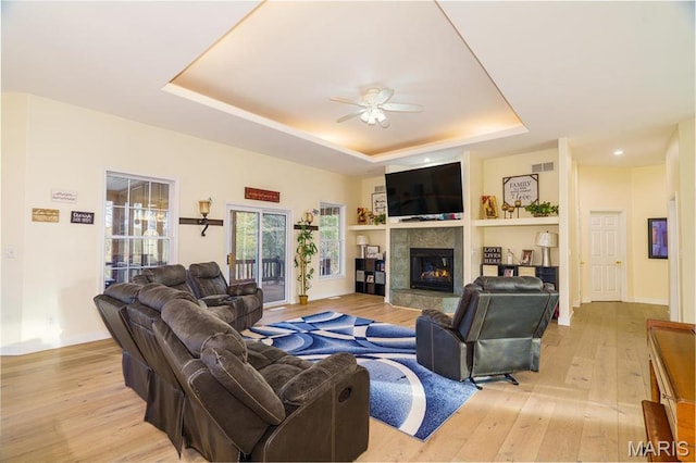 living room featuring a raised ceiling, a ceiling fan, light wood-type flooring, a fireplace, and baseboards