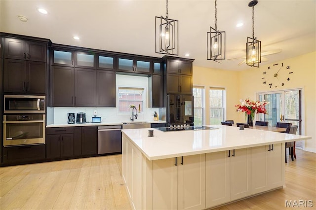 kitchen featuring stainless steel appliances, a sink, light countertops, light wood-type flooring, and a spacious island