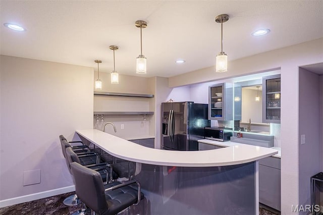 kitchen with fridge with ice dispenser, stainless steel microwave, a breakfast bar area, light countertops, and glass insert cabinets
