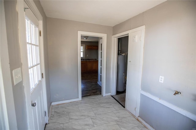 hallway featuring water heater, light marble finish floors, and baseboards
