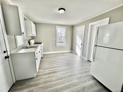 kitchen featuring white appliances, light countertops, light wood-style floors, a sink, and baseboards