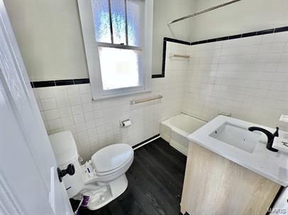 bathroom with tile walls, toilet, shower / bathtub combination, vanity, and wainscoting