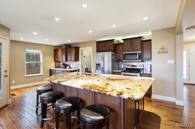 1500 Swiss Village Rd, Osage Beach, MO 65065 - kitchen with stainless steel appliances, hardwood / wood-style floors, a kitchen island with sink, a breakfast bar area, and dark brown cabinets