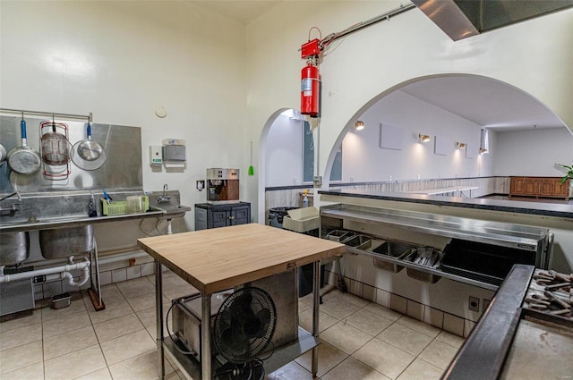 kitchen featuring arched walkways, light tile patterned floors, and a towering ceiling