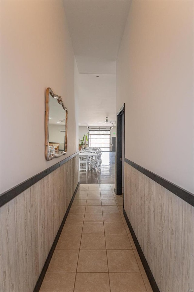 corridor featuring wainscoting, light tile patterned floors, and wood walls