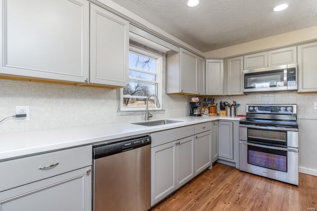 kitchen with appliances with stainless steel finishes, a sink, gray cabinetry, light wood-style flooring, and light countertops