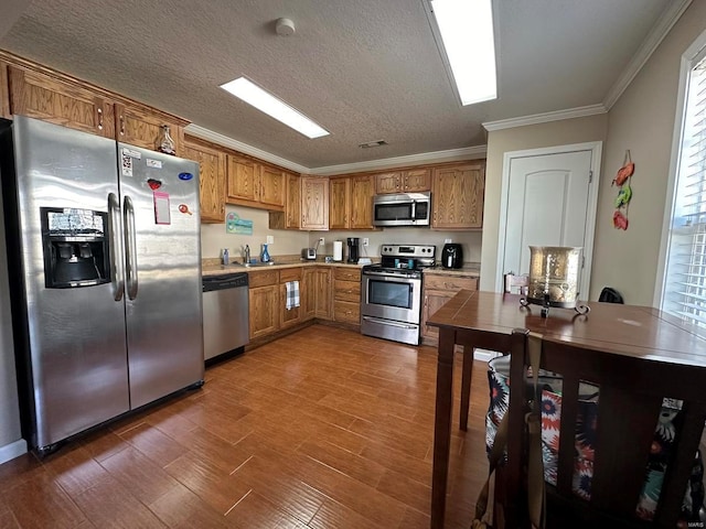 kitchen featuring appliances with stainless steel finishes, crown molding, a sink, brown cabinets, and dark wood-type flooring