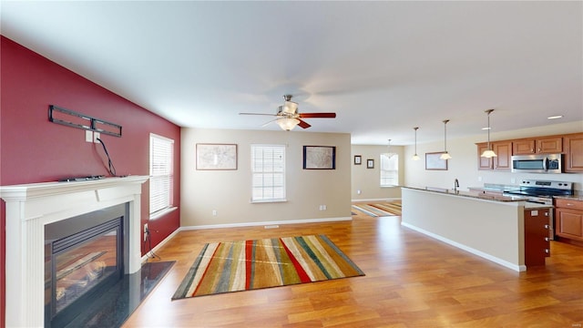 unfurnished living room featuring light wood-style flooring, a glass covered fireplace, a ceiling fan, baseboards, and a sink
