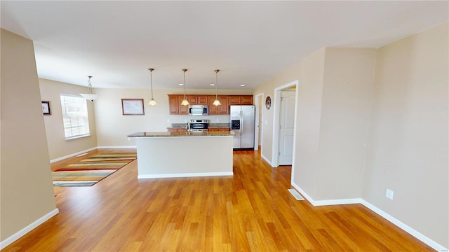 kitchen featuring stainless steel appliances, light wood-type flooring, baseboards, and brown cabinets