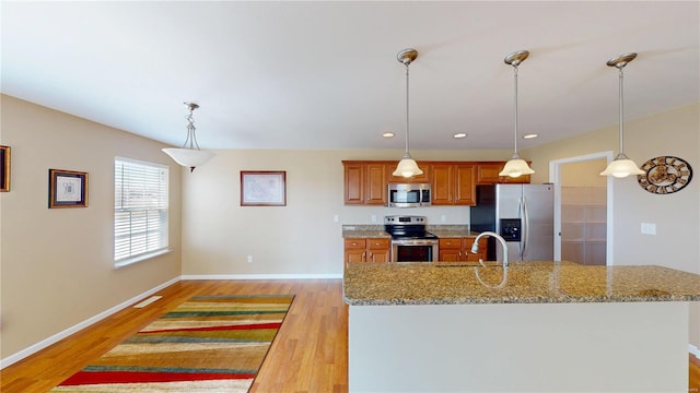 kitchen with appliances with stainless steel finishes, brown cabinets, light wood-type flooring, light stone countertops, and recessed lighting