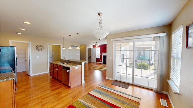 kitchen featuring a sink, appliances with stainless steel finishes, light wood-style floors, hanging light fixtures, and light stone countertops