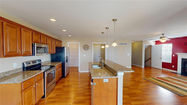 kitchen featuring stainless steel appliances, a sink, brown cabinetry, light wood-type flooring, and a kitchen island with sink