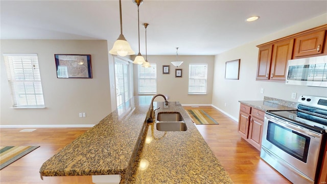 kitchen featuring appliances with stainless steel finishes, a sink, light wood-style flooring, dark stone countertops, and recessed lighting
