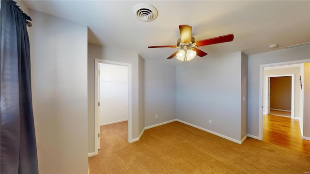 unfurnished bedroom with light colored carpet, baseboards, a walk in closet, and ceiling fan