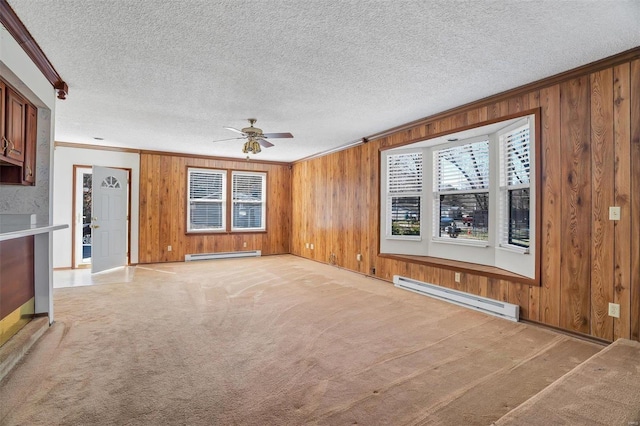 unfurnished living room with a baseboard radiator, ornamental molding, wooden walls, ceiling fan, and baseboards