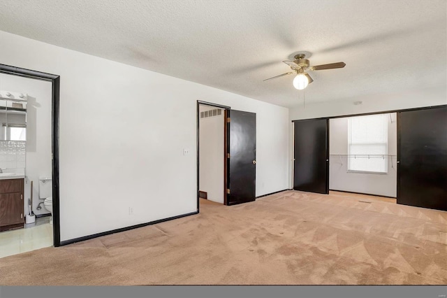 unfurnished bedroom with light colored carpet, ensuite bathroom, a textured ceiling, and a ceiling fan