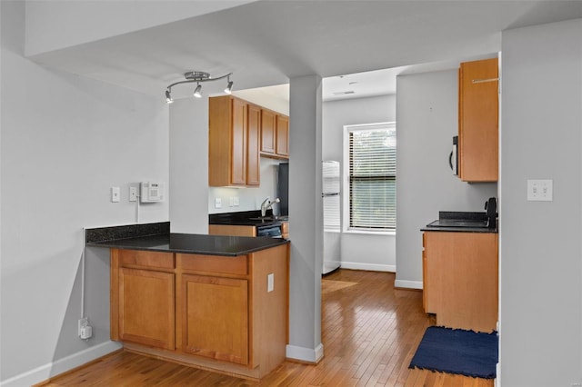 kitchen with a sink, light wood-style flooring, baseboards, and dark countertops