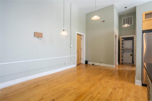 empty room featuring a towering ceiling, light wood finished floors, and baseboards