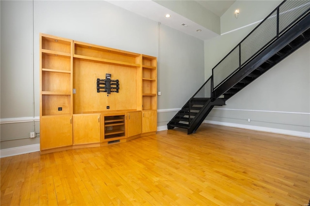 unfurnished living room featuring hardwood / wood-style flooring, stairs, baseboards, and recessed lighting