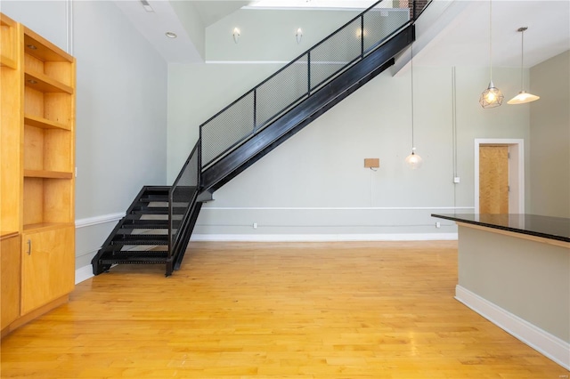 stairs with wood finished floors, a towering ceiling, and baseboards