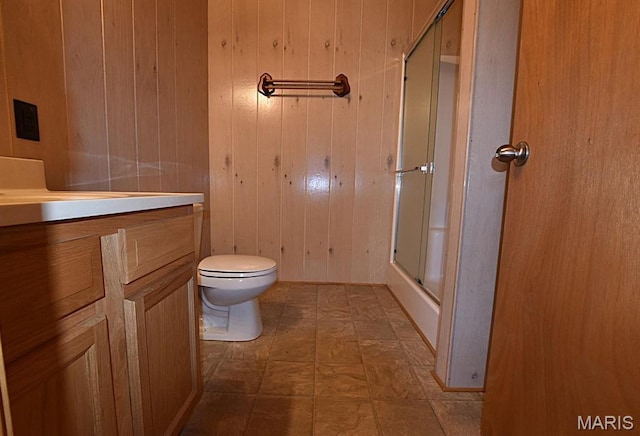 bathroom featuring an enclosed shower, vanity, wooden walls, toilet, and tile patterned floors