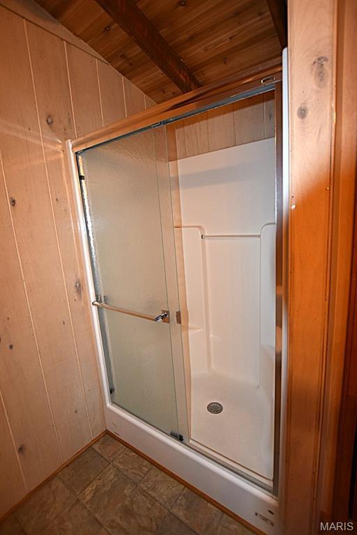 full bathroom with wood ceiling, a stall shower, beamed ceiling, and wood walls