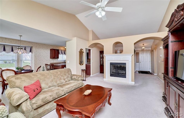 living room featuring ceiling fan, arched walkways, light colored carpet, high vaulted ceiling, and a glass covered fireplace