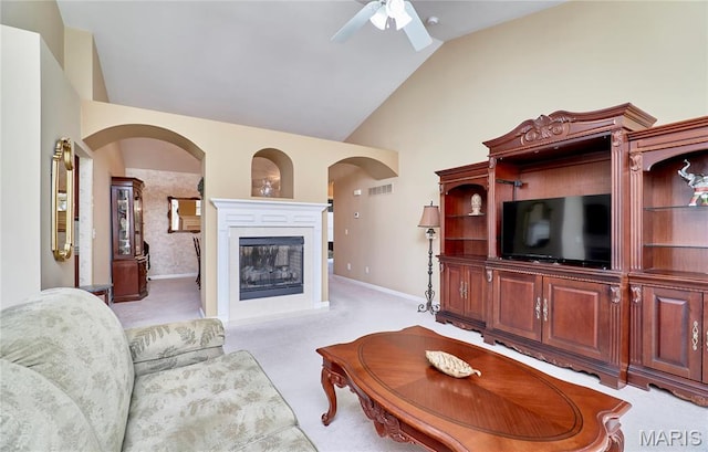 living room with vaulted ceiling, ceiling fan, arched walkways, a glass covered fireplace, and light carpet